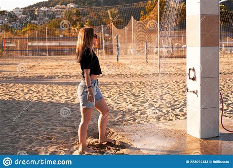 A Girl In Shorts And A Black T Shirt On The Beach Near The Shower