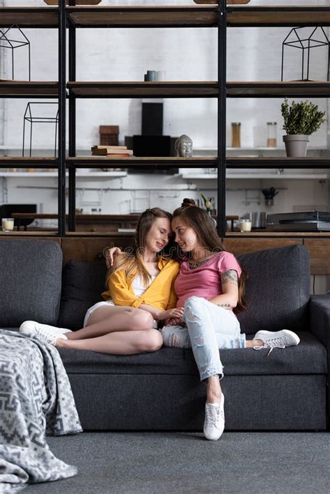 Two Pretty Lesbians Embracing While Sitting On Sofa In Living Room