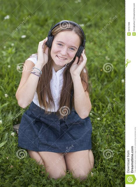 cute teen girl in headphones enjoys the music on the green grass in park love of music stock
