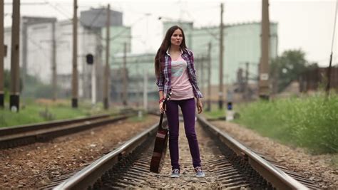 a beautiful latina brunette walks away from the camera down a lonely stretch of railroad track