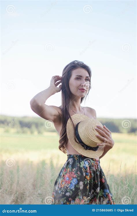 topless brunette woman covering her breasts with straw hat in the field