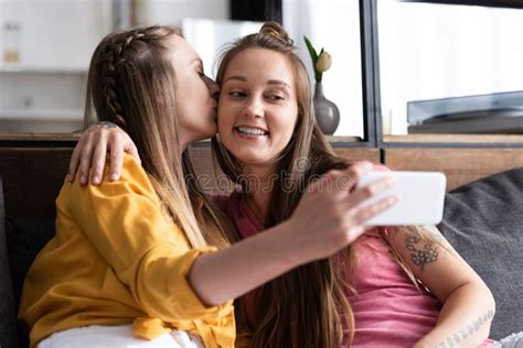 Lesbian In Yellow Blouse Kissing Girlfriend While Taking Selfie Stock