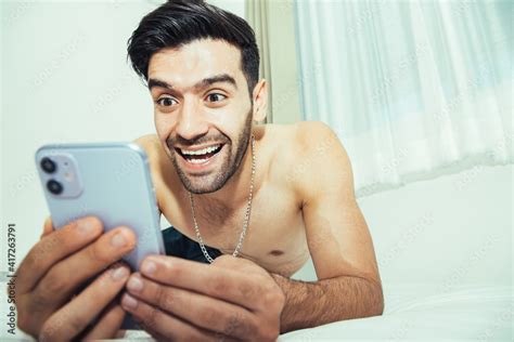 Handsome Shirtless Man On Bed With Intense Face Expression Using Mobile