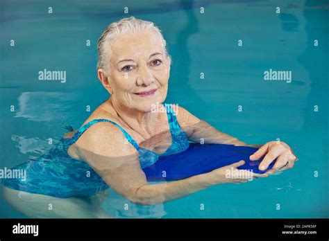 Smiling Senior Woman Makes Aqua Fitness With Swimming Board In The