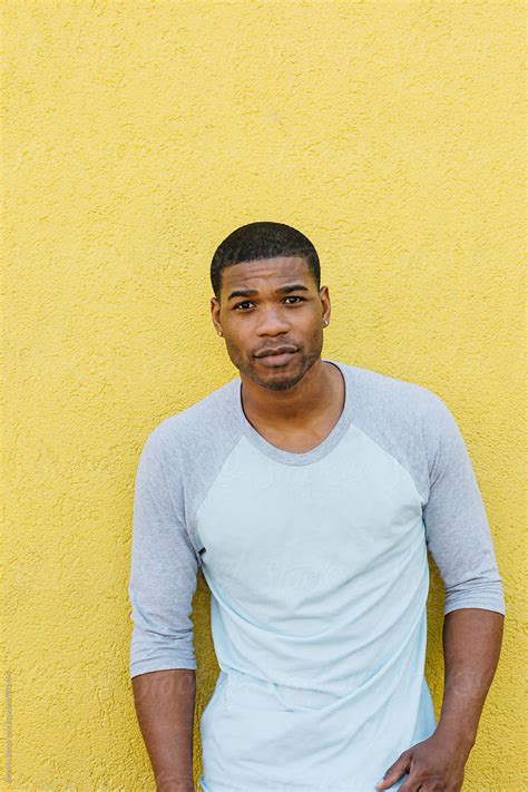 african american man standing in front of a yellow wall by stocksy