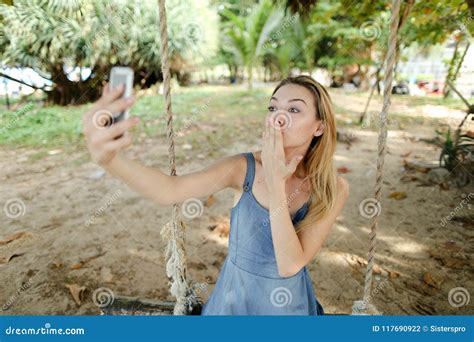 Young Jocund Girl Riding Swing And Making Selfie By Smartphone Sand