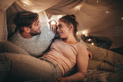 Happy Man And Woman Lying On Bed Talking While Looking At Each Other