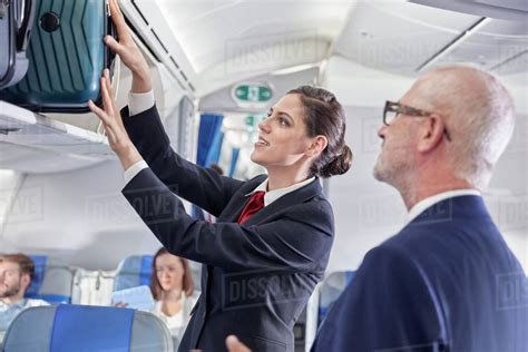 flight attendant helping businessman place luggage  overhead compartment  airplane stock