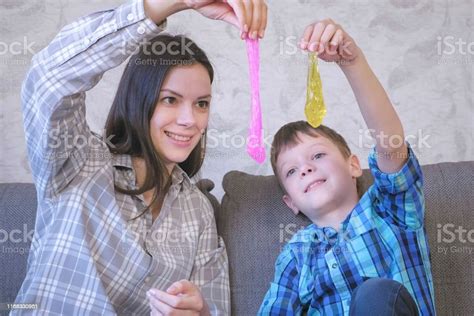 Happy Mom And Son Are Playing With Slime Sitting On The Sofa Stretching
