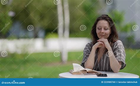 teacher woman is sitting at table outdoors in park reading book and