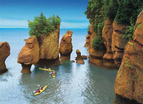 people  kayaks paddling   water  large rock formations  trees