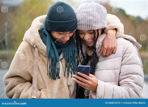 Happy Dominican Lesbian Couple Using The Phone At Street In Winter