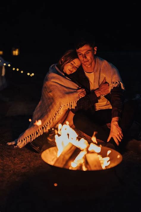 a man and woman sitting next to a campfire at night with lights on the