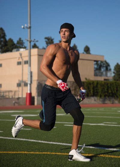 a shirtless man running on a football field with his gloved hand in the air
