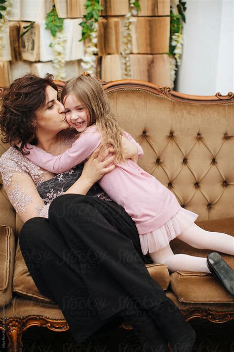 mother and daughter cuddling and kissing each other indoors by liliya