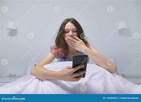 tired teenager girl sitting at home in bed looking at mobile phone