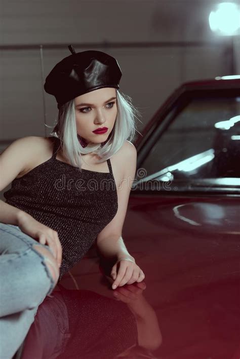 Beautiful Blonde Woman In Black Beret Lying On Maroon Car And Looking