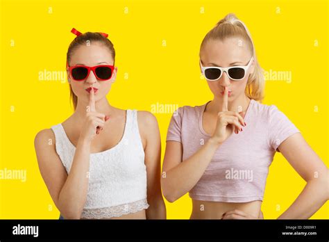 Portrait Of Two Playful Young Women With Fingers On Lips Over Yellow