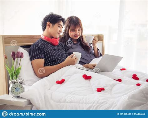 attractive couple sitting on bed holding cups of coffee