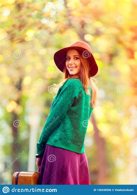 beautiful redhead girl with suitcase in the park stock