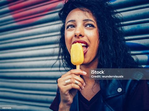 Urban Teen Girl Licking An Orange Colored Flavoured Ice Lolly Stock
