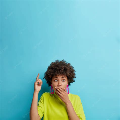 premium photo shocked curly haired woman covers mouth points index