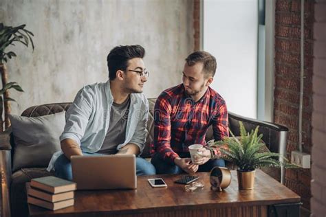 european gay male couple spend time together drinking coffee and watching laptop stock image