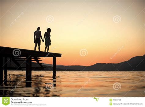 silhouette of sensual couple stand on pier with sunset
