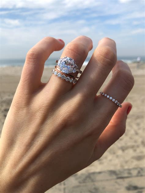 A Womans Hand With Two Rings On It And The Beach In The Background