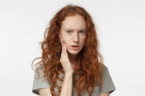Indoor Portrait Of Redhead Girl Feeling Pain Holding Her Cheek With