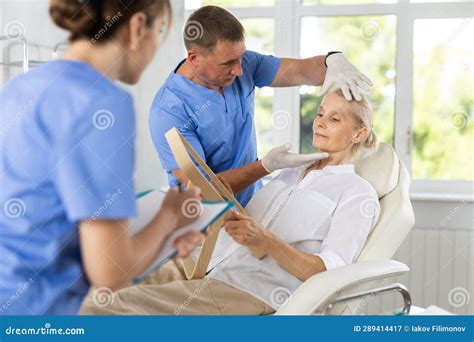 Male Beautician Together With A Nurse Examines The Face Of An Mature