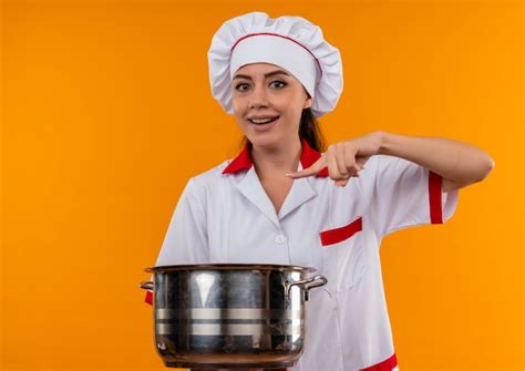 photo young joyful caucasian cook girl  chef uniform holds  points  pot isolated