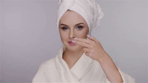 pretty girl in bathrobe and bath towel applying cream on face stock