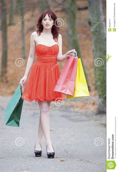 girl in red dress with shopping bags walking in park sale and retail