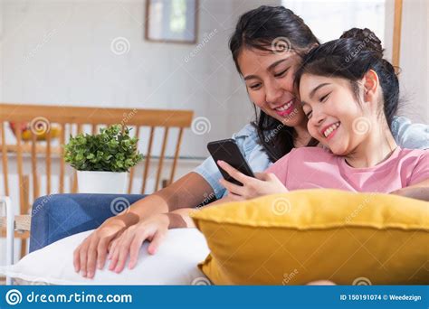 Happy Asian Lesbian Watching Video On Mobile Phone At Sofa In House