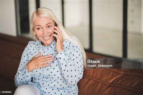 Blonde Mature Woman Talking On The Phone While Sitting On The Sofa