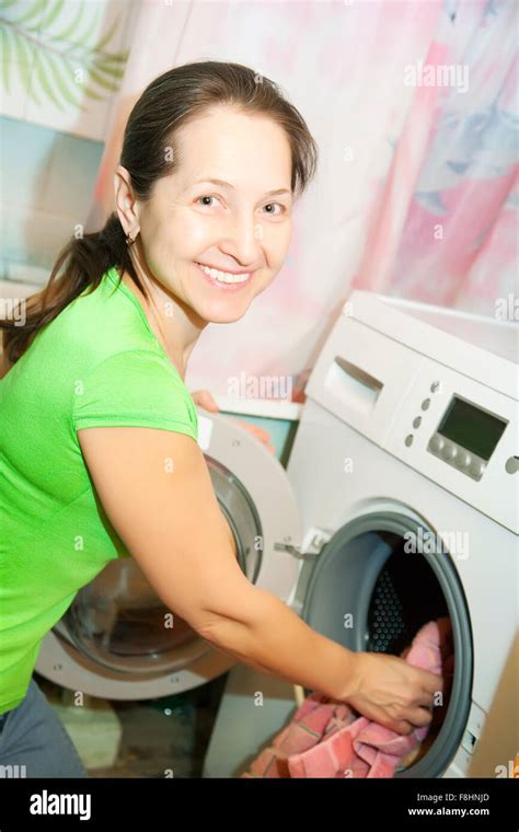 Mature Woman Putting Clothes In To Washing Machine And Smiling Stock