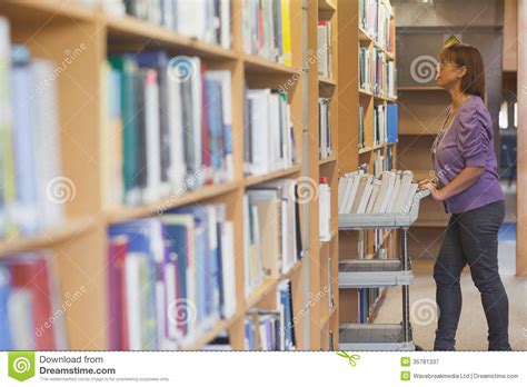 Mature Female Librarian Pushing A Cart In Library Royalty