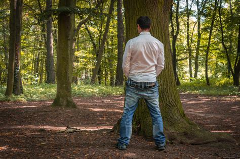 Standing Man Peeing Near Big Tree In Autumn Forest Stock