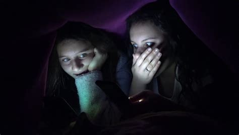 4k sleepy teen friends sneak surf on tablet smartphone hidden under bed blanket uhd stock