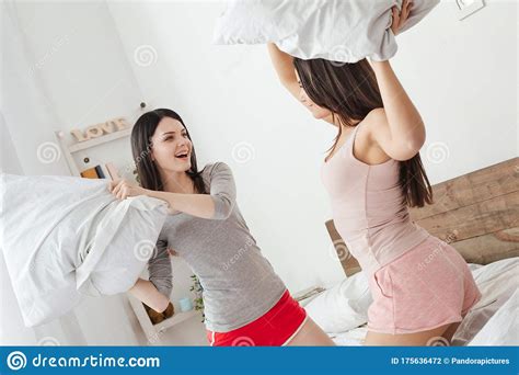 Lesbian Couple In Bedroom At Home On Bed Fighting With Pillows Excited