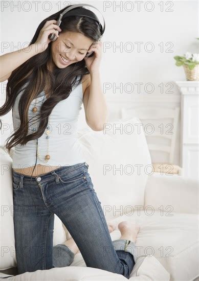 Asian Woman Wearing Headphones And Kneeling On Sofa Photo12 Tetra