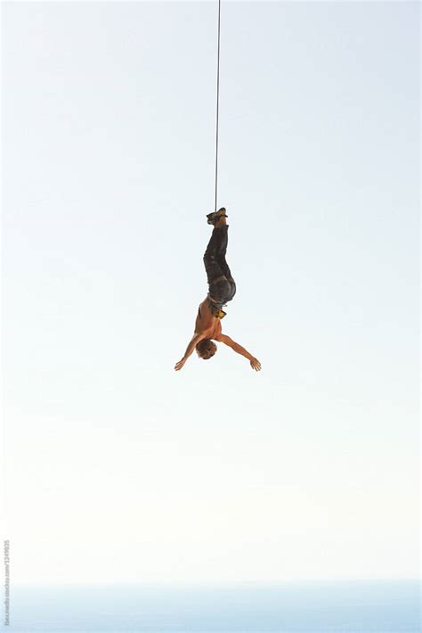 man hanging upside   arms spread    rope  stocksy