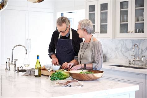 Mature Couple With Grey Hair Cooking In Kitchen Of Luxury Home By