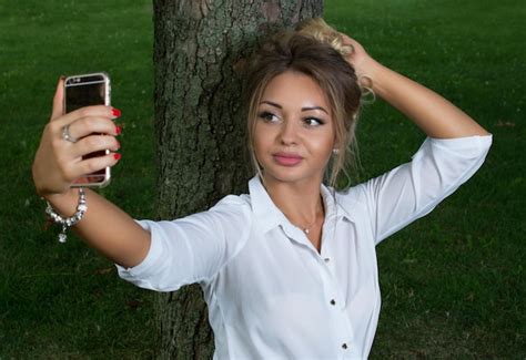 premium photo portrait of a girl in a white shirt doing selfie in a park
