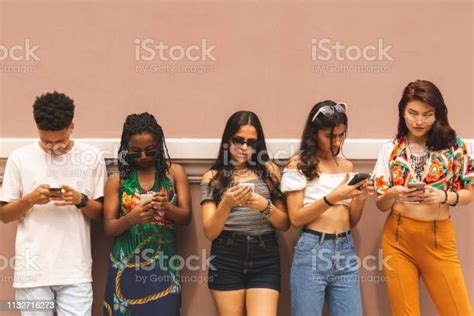 Group Of Multi Ethnic Latin Teenagers Using Smartphone Outdoors Stock