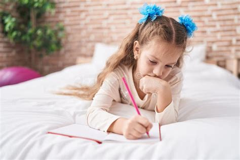 Adorable Caucasian Girl Writing On Notebook Lying On Bed At Bedroom
