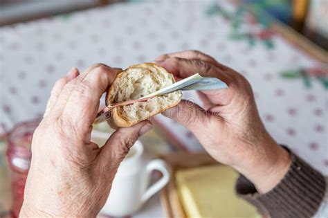 Old Woman Granny Pensioner Sits At Set Breakfast Table Eating A Roll