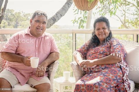 Mature Aboriginal Couple Sitting On Chairs And Smiling Towards Camera