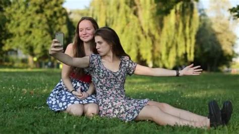 Two Cheerful Cute Girlfriends Do Selfie On The Phone Sitting On The